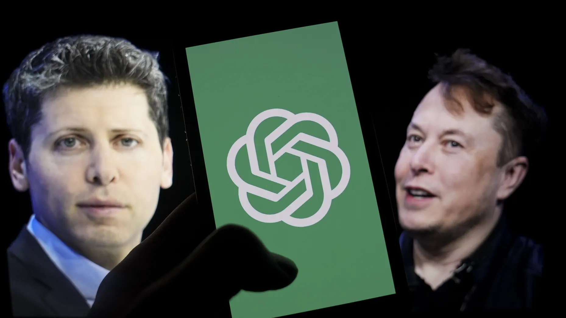 The logo of OpenAI is shown on a mobile phone in front of a computer screen displaying the photographs of Sam Altman, left, and Elon Musk,